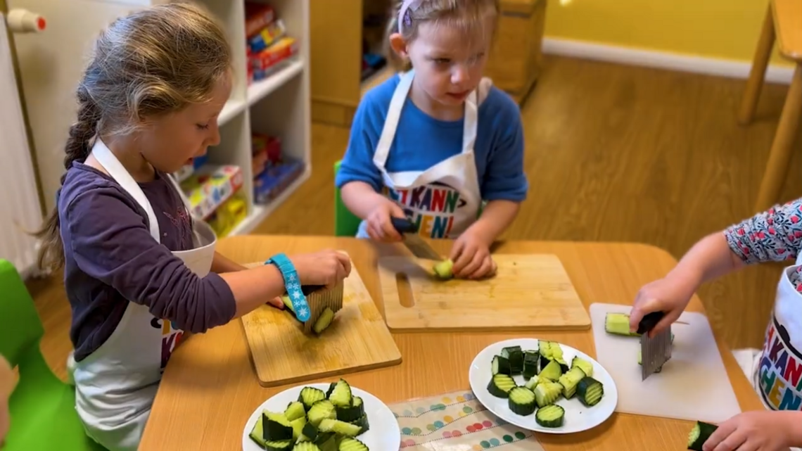 Kinder an einem Tisch schneiden Gurken