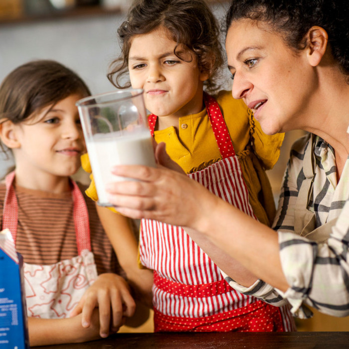 Mutter misst mit ihren Töchtern Milch in der Küche ab.