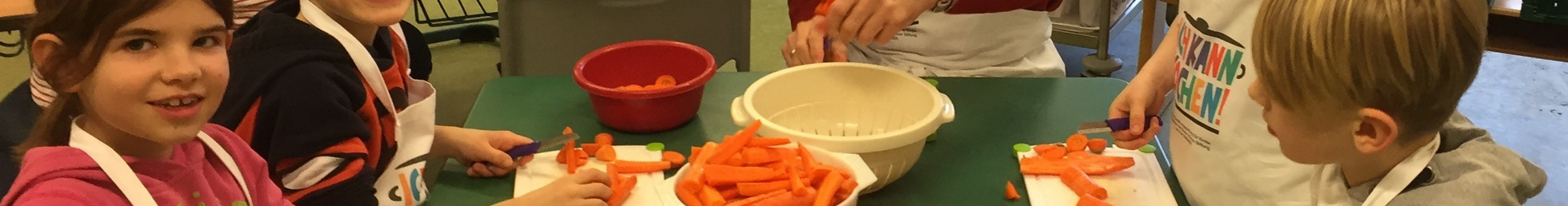 Kinder schneiden gemeinsam Gemüse, das sie in ihrem Schulgarten geerntet haben.